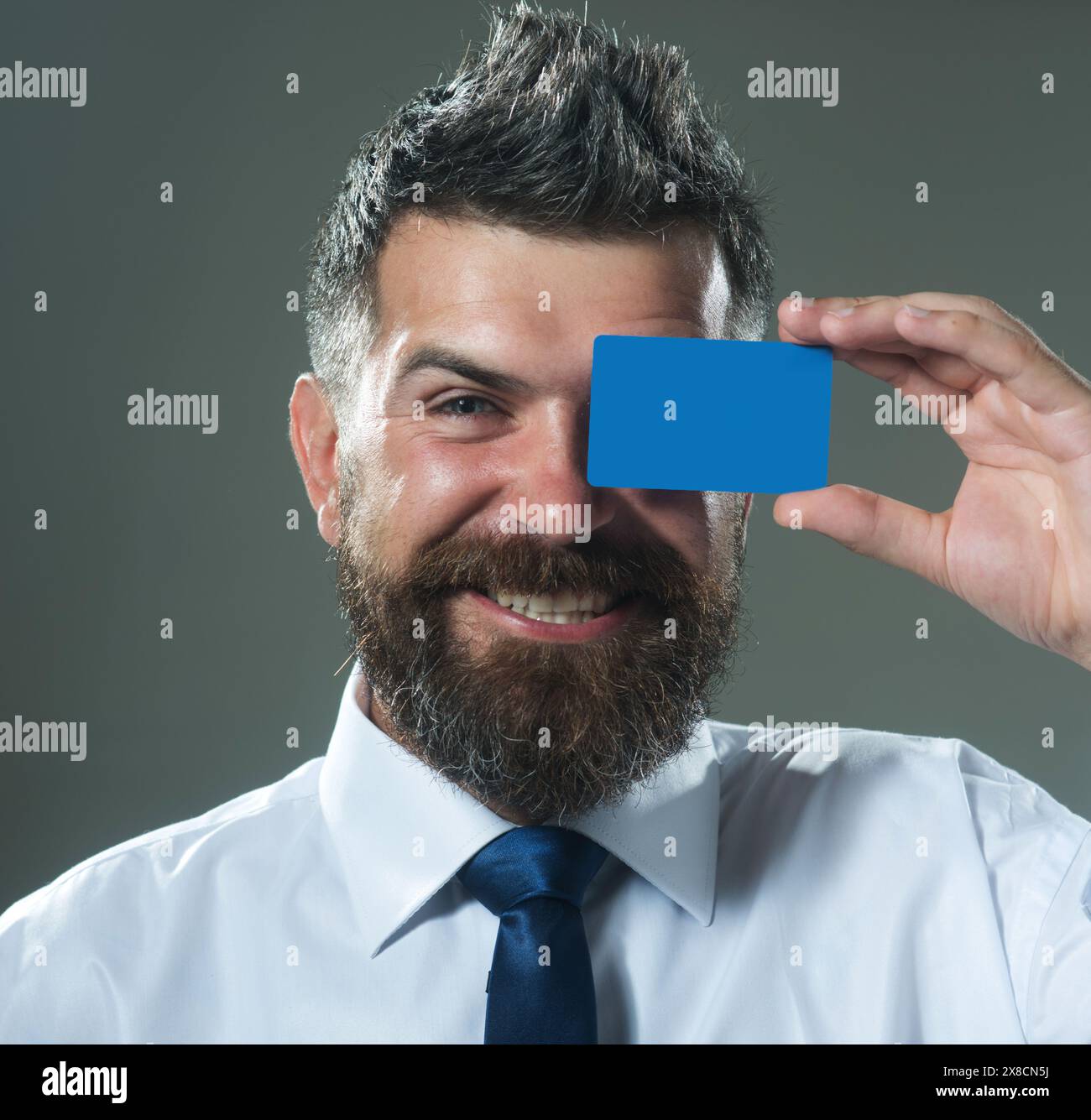 Uomo sorridente con barba che copre l'occhio con un mockup vuoto biglietto da visita vuoto. Bell'uomo d'affari con carta di credito o di debito. Uomo barbuto felice dentro Foto Stock