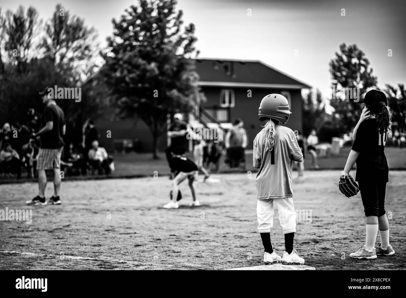 Due giovani ragazze di softball alla prima base con allenatore deconcentrato e squadra in background. Foto Stock