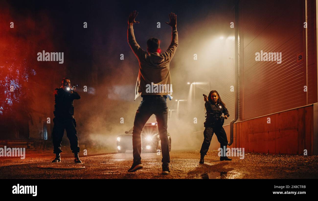 Due agenti di polizia puntano a un Fellon. Poliziotti che usano un'arma per intimidire il sospetto. Fellon che alza la mano nella conformità. Eroiche forze dell'ordine che arrestano un uomo pericoloso. Scatto simmetrico Foto Stock