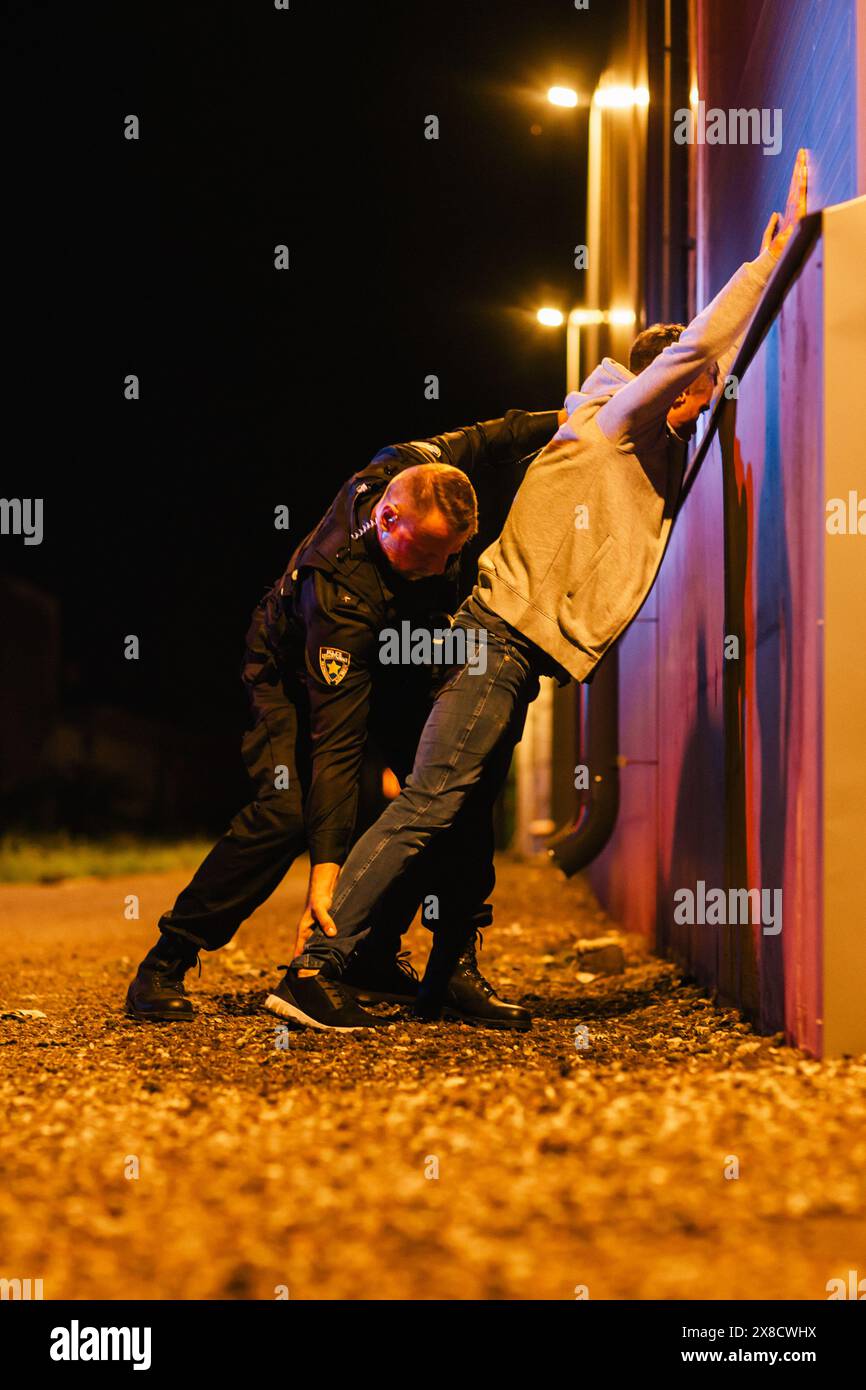 Un poliziotto professionista di mezza età che esegue una ricerca Pat-Down su un Fellon in Empty Back Alley. Un documentario come Shot of Procdure di arrestare i sospettati. Poliziotto esperto in cerca di armi Foto Stock