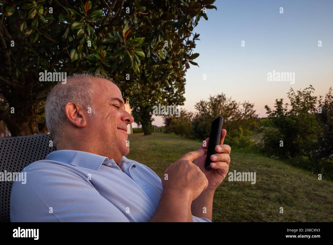 adulto maschio bianco che riposa in giardino con cellulare in mano che parla al tramonto Foto Stock