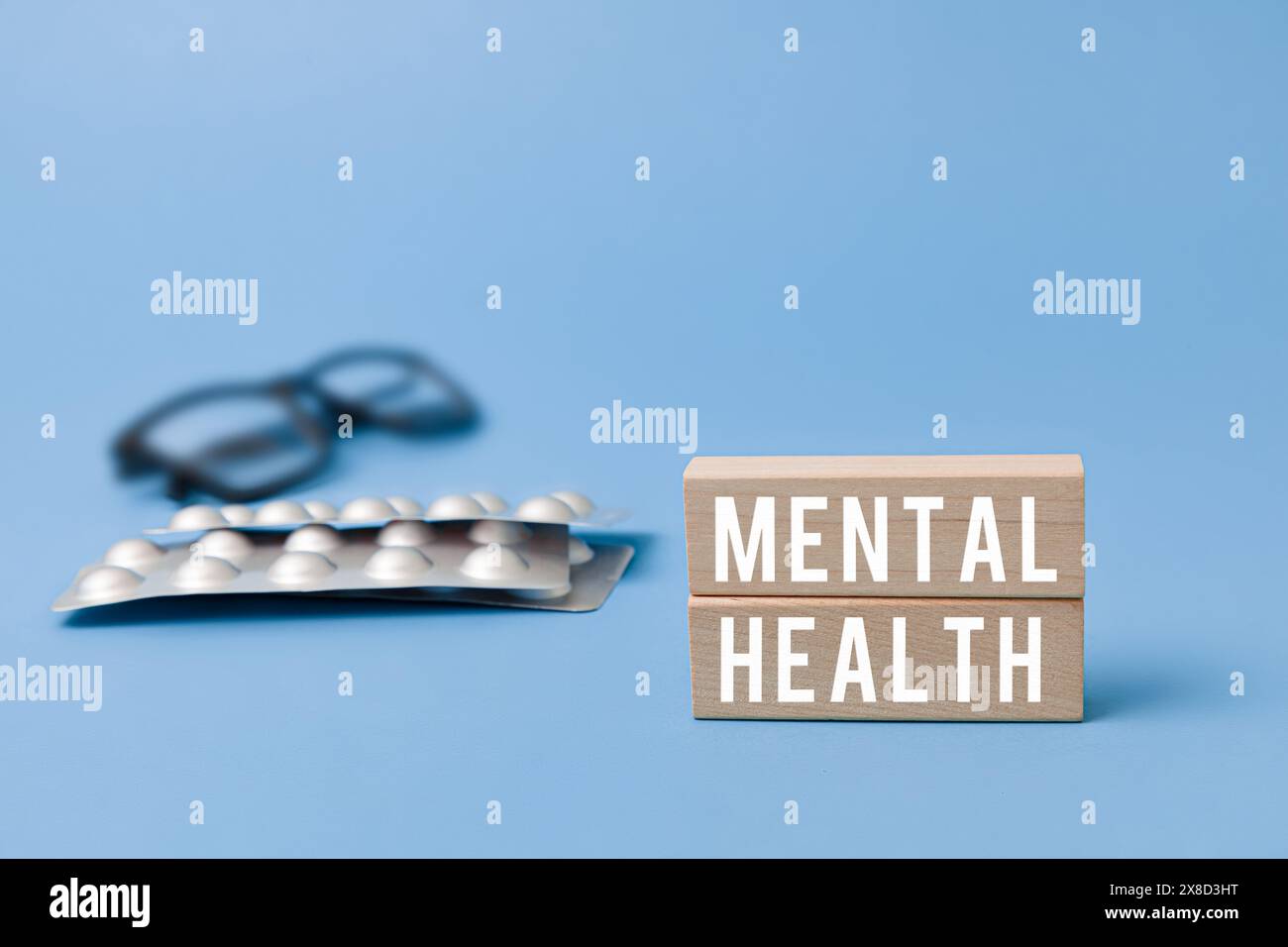 Concetto di salute mentale: Con blocco di legno; bicchieri e pillole su sfondo blu. Rappresentazione simbolica del benessere mentale e del trattamento. Foto Stock