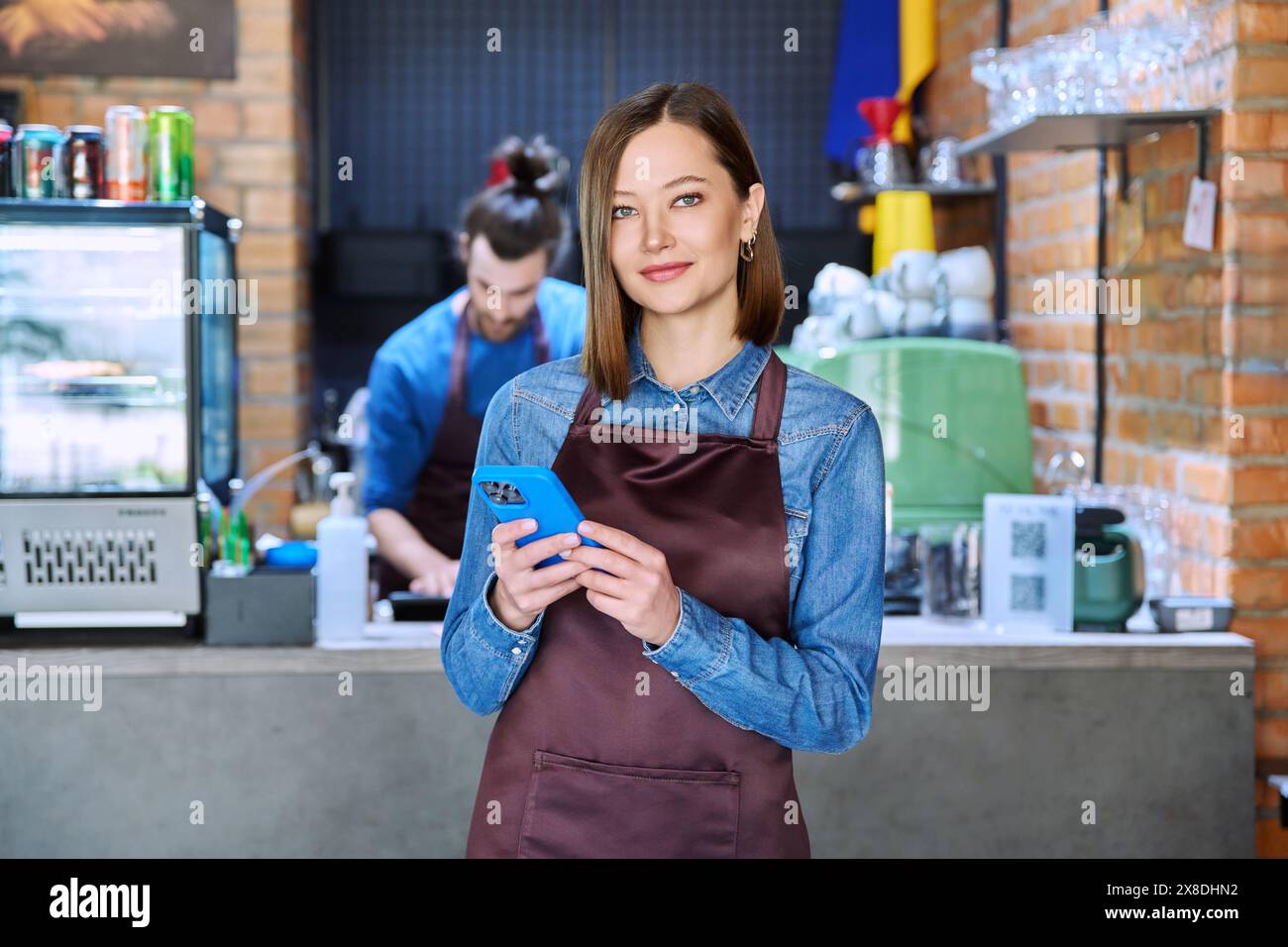 Giovane lavoratrice di servizio in grembiule con smartphone nel ristorante e nella caffetteria Foto Stock