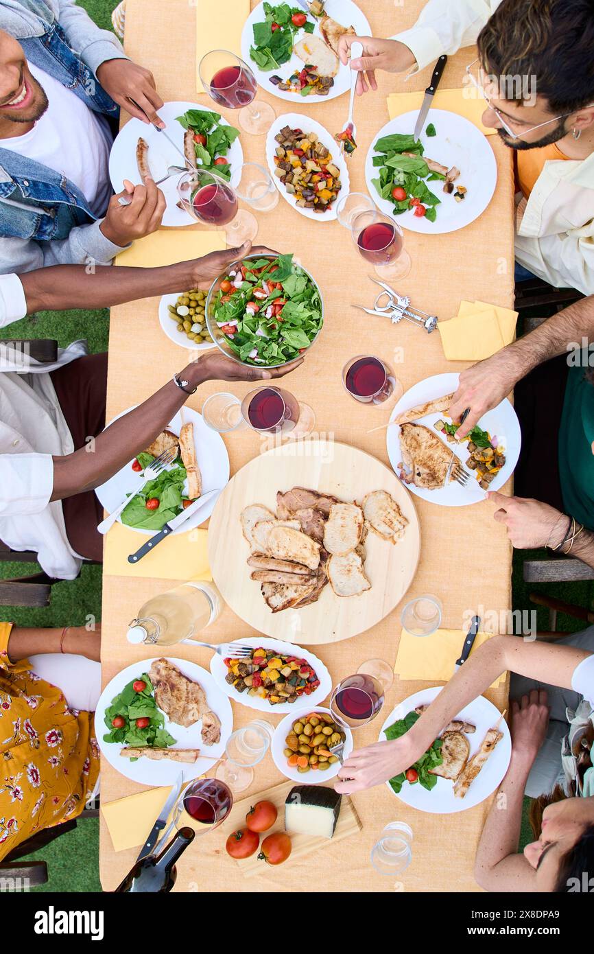 Vista dall'alto delle persone irriconoscibili intorno al tavolo del barbecue con bicchieri da vino e cibo all'aperto. Foto Stock