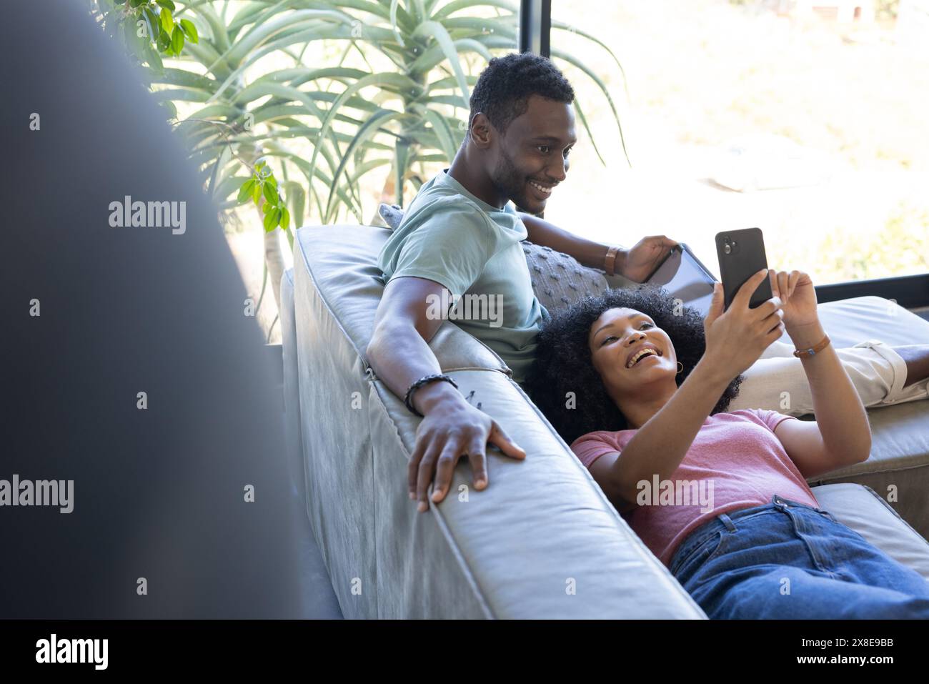 Una coppia variegata che si rilassa a casa, la moglie mostra lo smartphone al marito Foto Stock