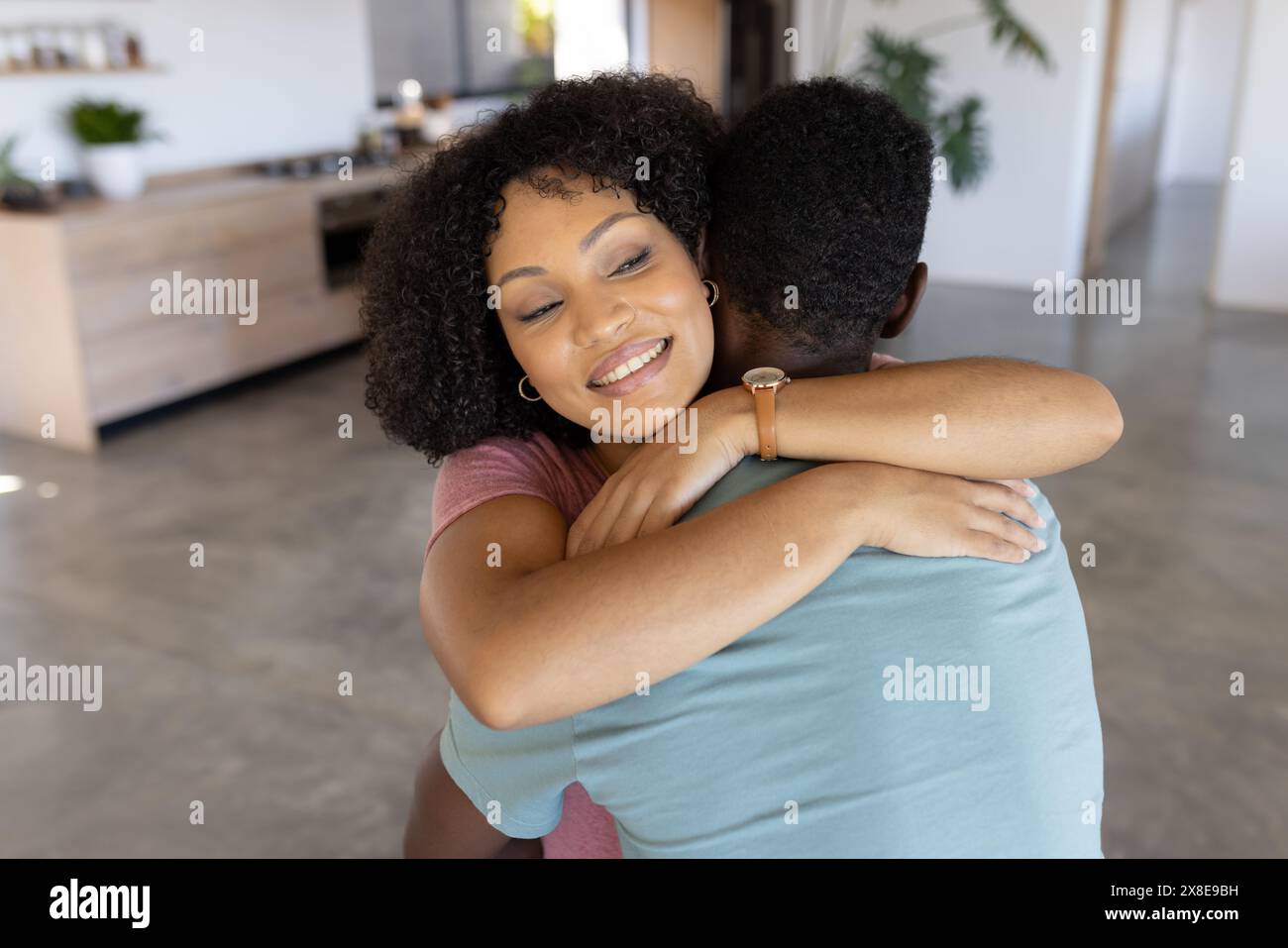 Coppie diverse che si abbracciano a casa, entrambe sorridenti Foto Stock