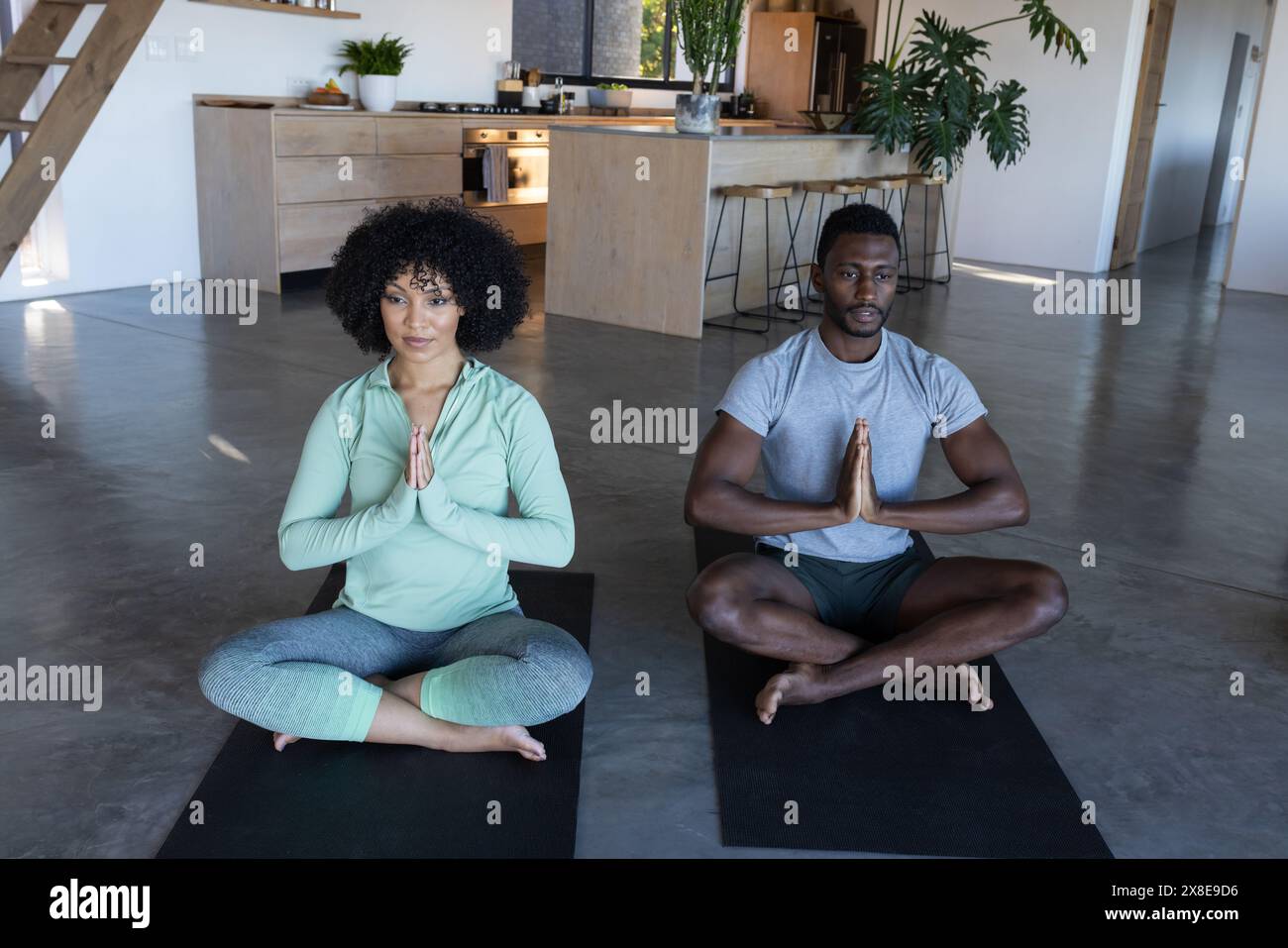 Una coppia variegata che meditava a casa, indossando abiti casual Foto Stock