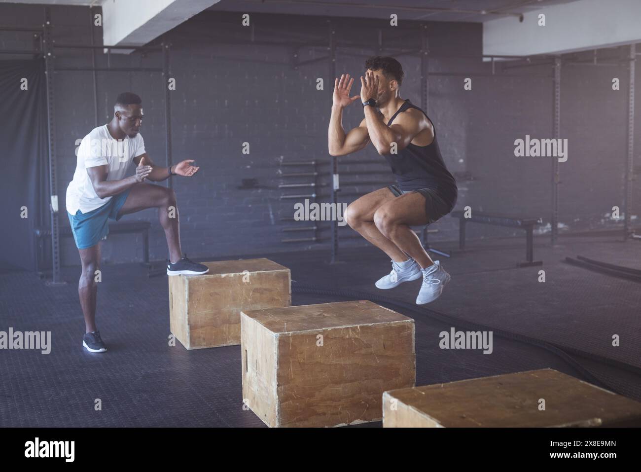 In palestra, diversi uomini si allenano con scatole di legno in una spaziosa palestra in stile industriale. Varie attrezzature fitness in background, inalterate Foto Stock