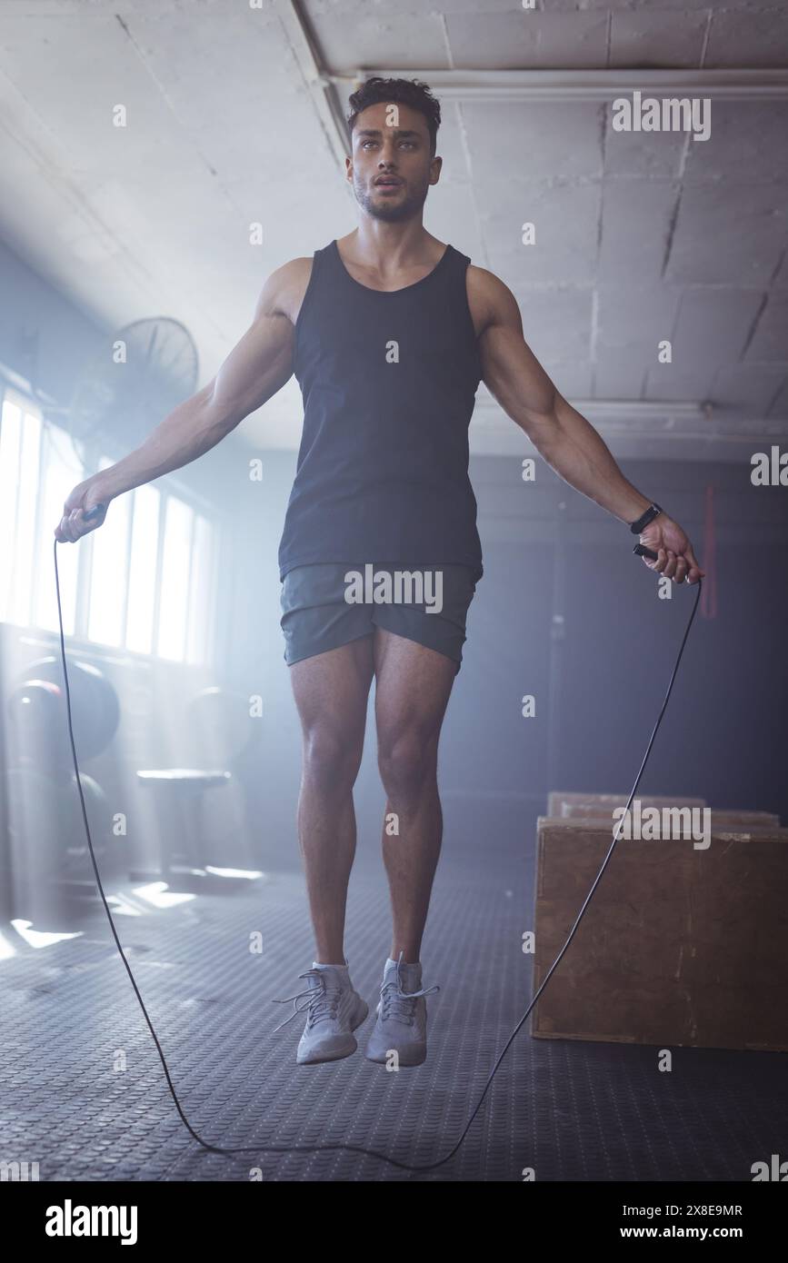 In palestra, un giovane uomo birazziale che salta la corda, sembra forte e in forma Foto Stock