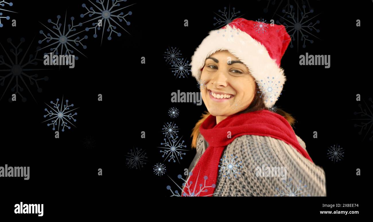 Immagine di una donna caucasica felice che indossa il berretto di babbo natale e che soffia il bacio contro i fiocchi di neve Foto Stock