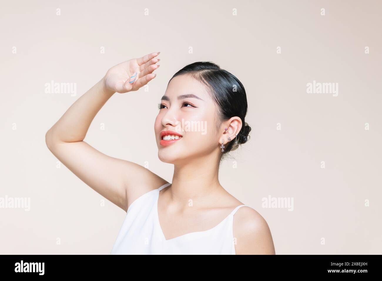 Bella giovane donna asiatica alzare le braccia per coprire il sole con una pelle fresca pulita su sfondo beige. Foto Stock