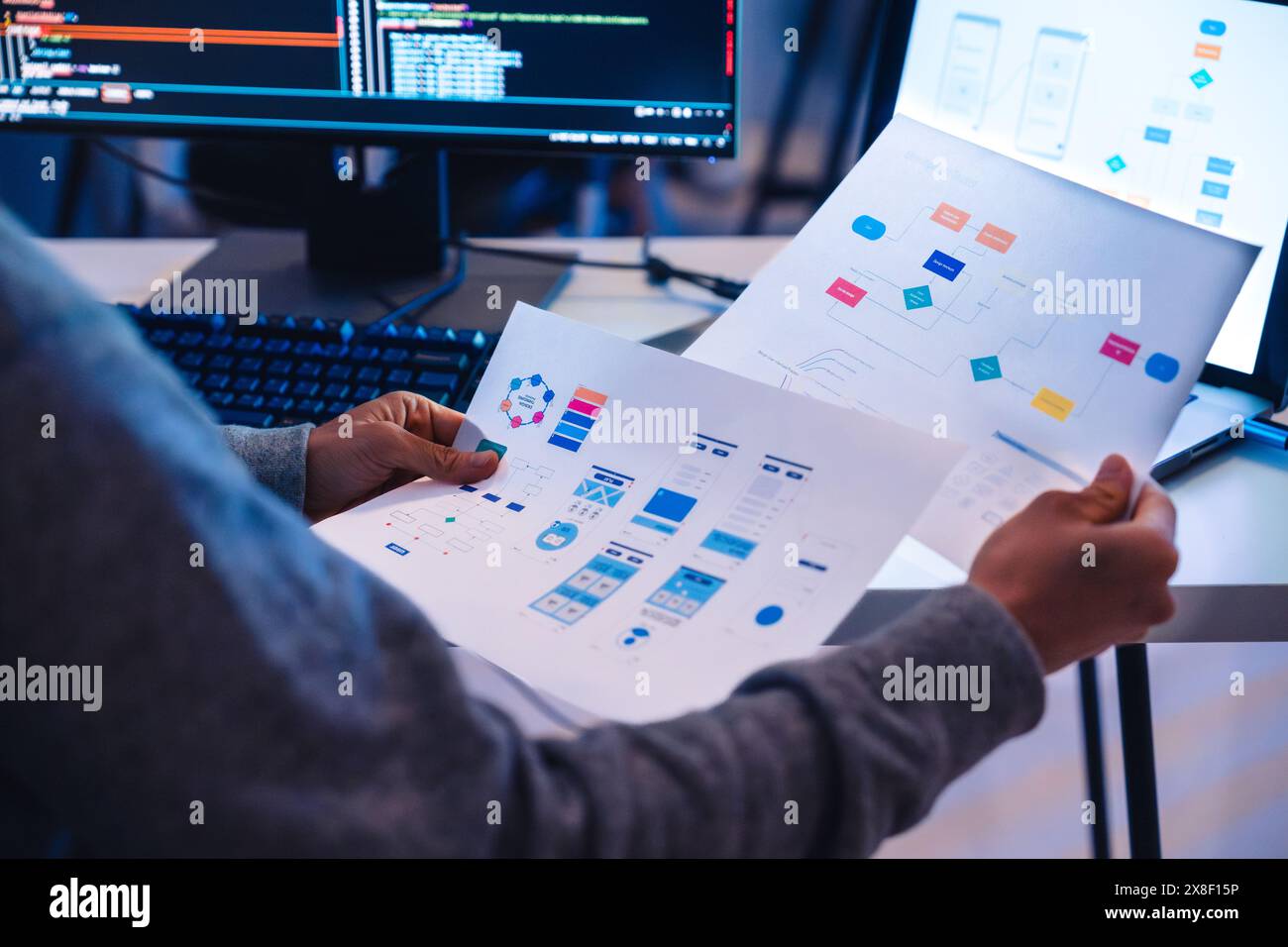 Lo sviluppatore software esamina i diagrammi di progettazione UX/UI durante la codifica su una workstation Foto Stock