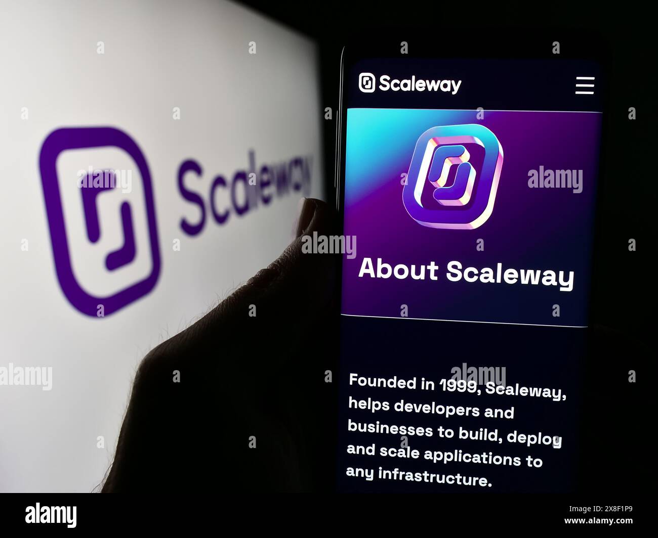 Persona che detiene lo smartphone con il sito Web dell'azienda francese di cloud computing Scaleway SAS davanti al logo. Messa a fuoco al centro del display del telefono. Foto Stock