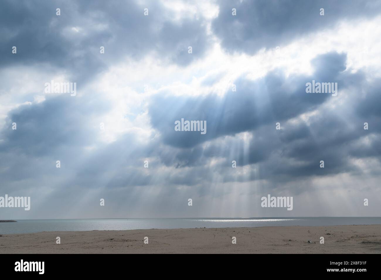 Spettacolari raggi del sole che penetrano attraverso la pesante copertura nuvolosa per illuminare la tranquilla spiaggia. Foto Stock