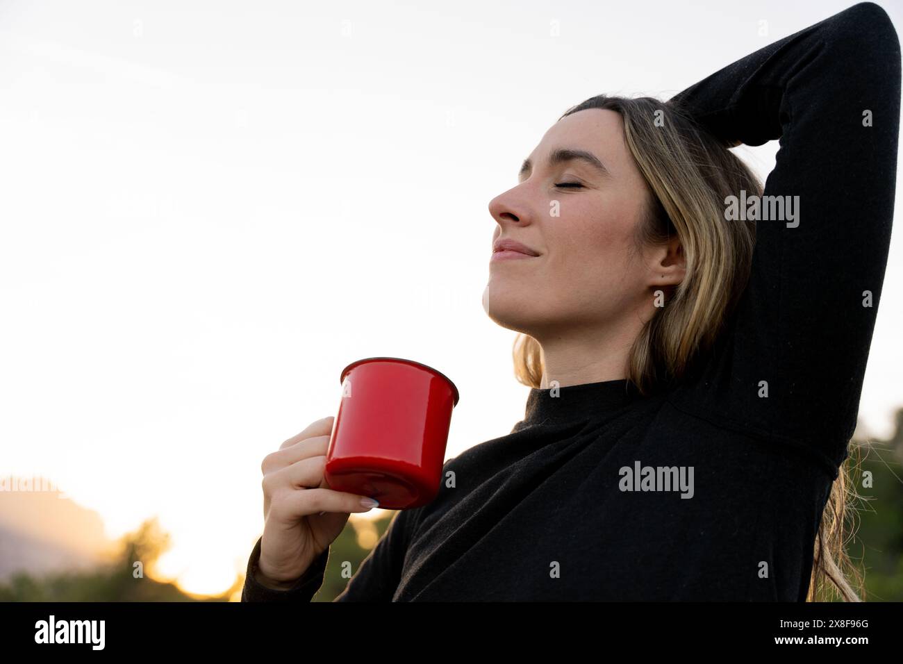 Donna che beve una tazza di caffè al mattino circondato dalla natura Foto Stock