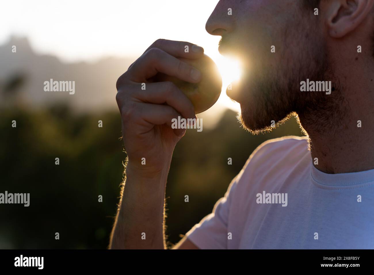 Giovane che mangia un pezzo di frutta al tramonto. Luce dorata riflesso del sole. Stile di vita sano e nutrizione. Spuntino sano Foto Stock