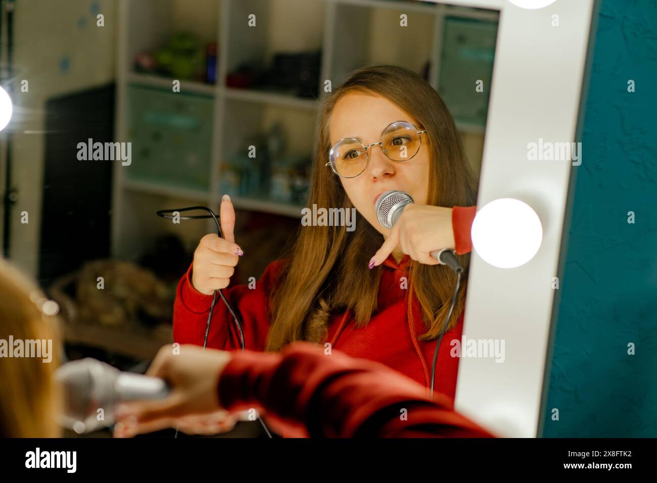 Donna che canta nel microfono mentre guarda Mirror at Home la sera. Foto Stock