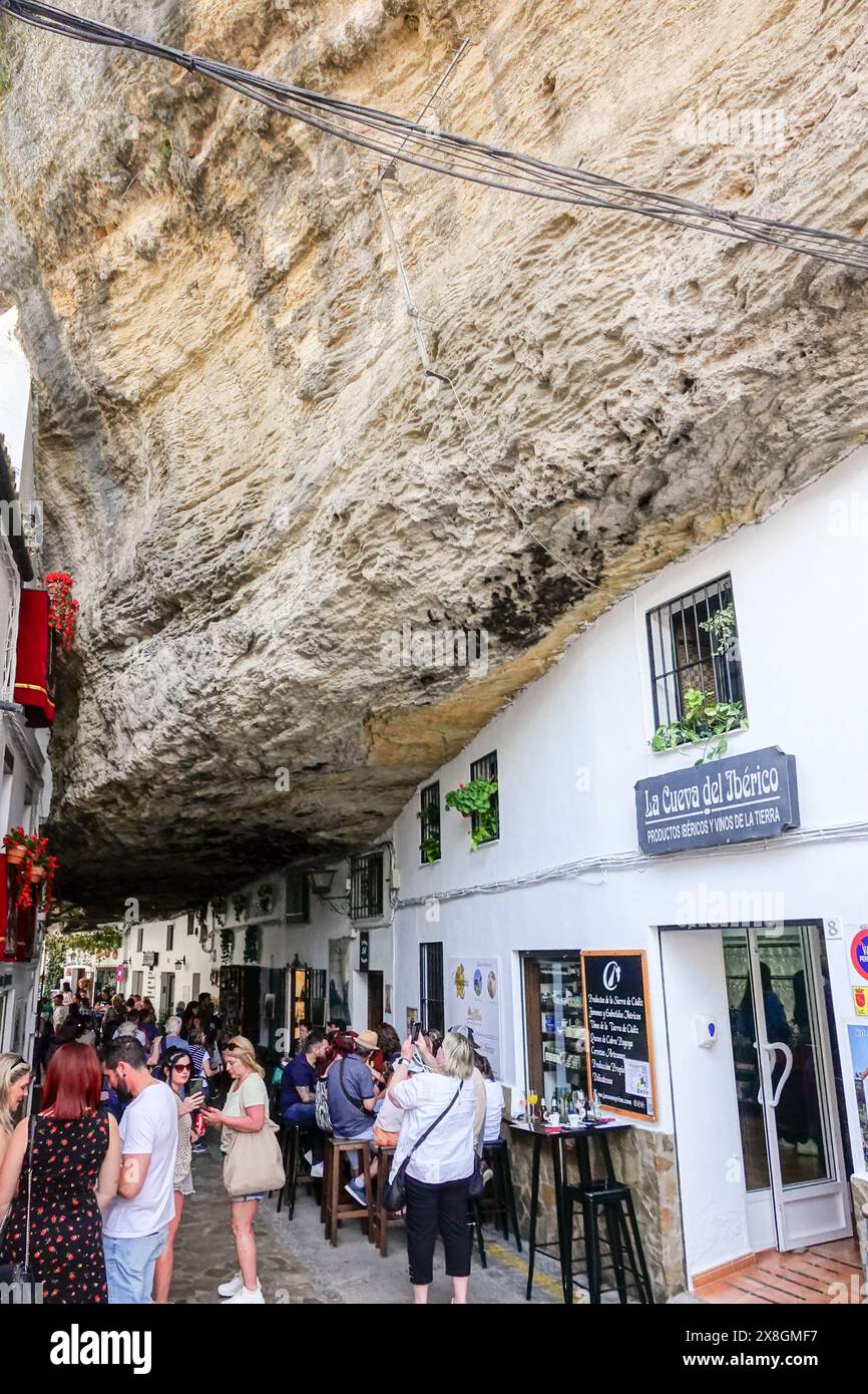 Ristoranti e caffetterie affollano lungo la Calle Cuevas de la Sombra sotto la sporgenza di roccia nel pueblos blanco unico di Setenil de las Bodegas, Spagna. I residenti del piccolo villaggio di Setenil hanno vissuto in case rupestri fin dal neolitico. Foto Stock