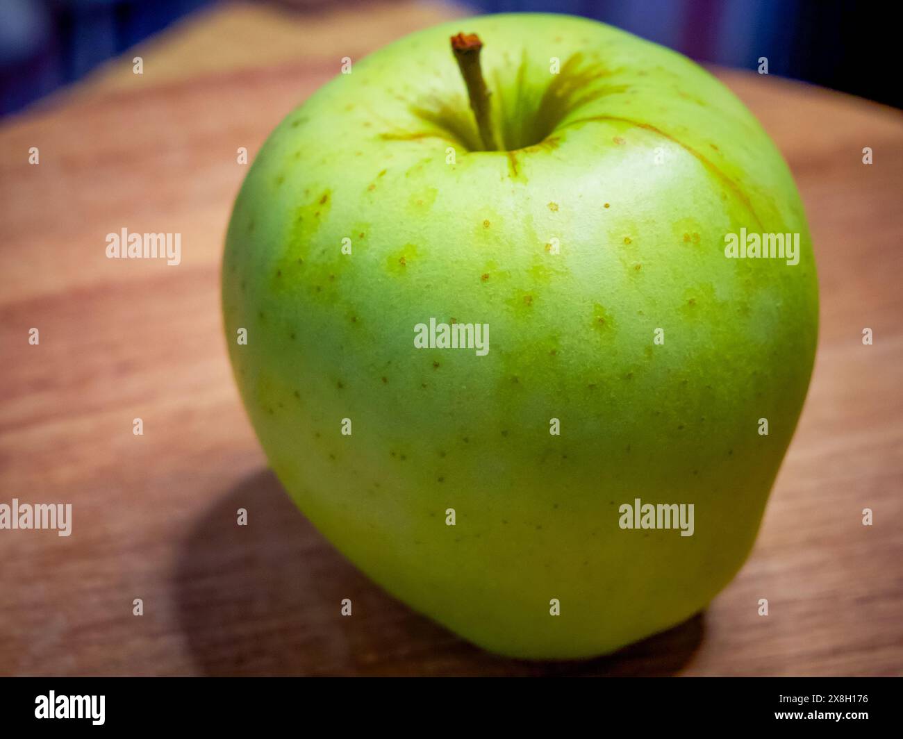 Una mela verde con un gambo su una superficie di legno, che indica freschezza e salute. Foto Stock