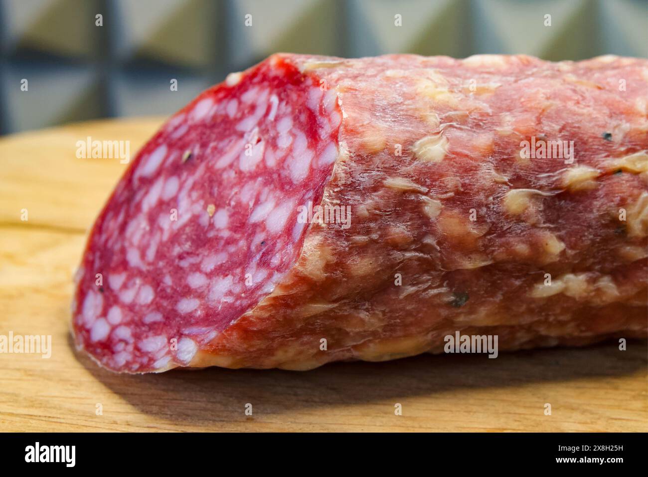 Un pezzo di salame su una tavola di legno, che ne sottolinea la consistenza e l'idoneità al contenuto culinario. Foto Stock