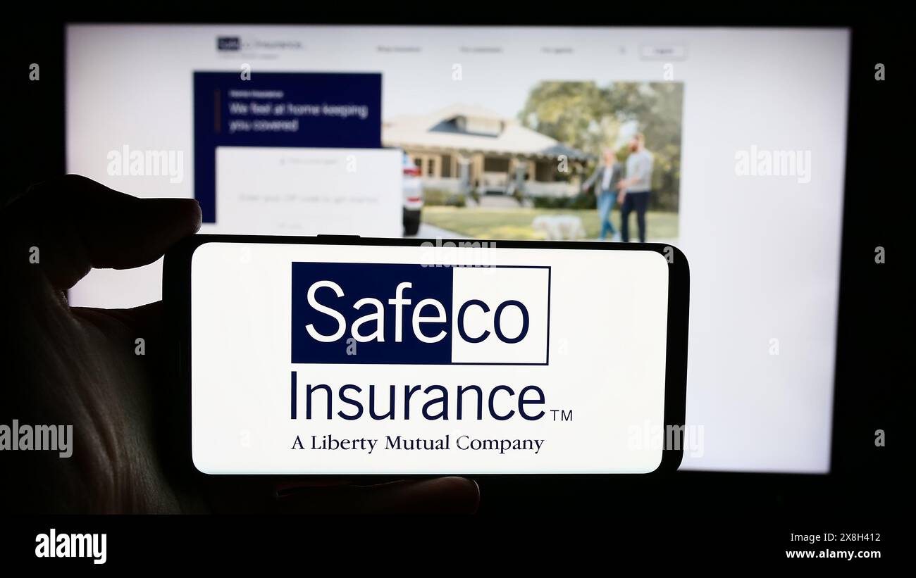 Persona che detiene un cellulare con il logo della società statunitense di servizi finanziari Safeco Insurance davanti alla pagina web aziendale. Mettere a fuoco il display del telefono. Foto Stock