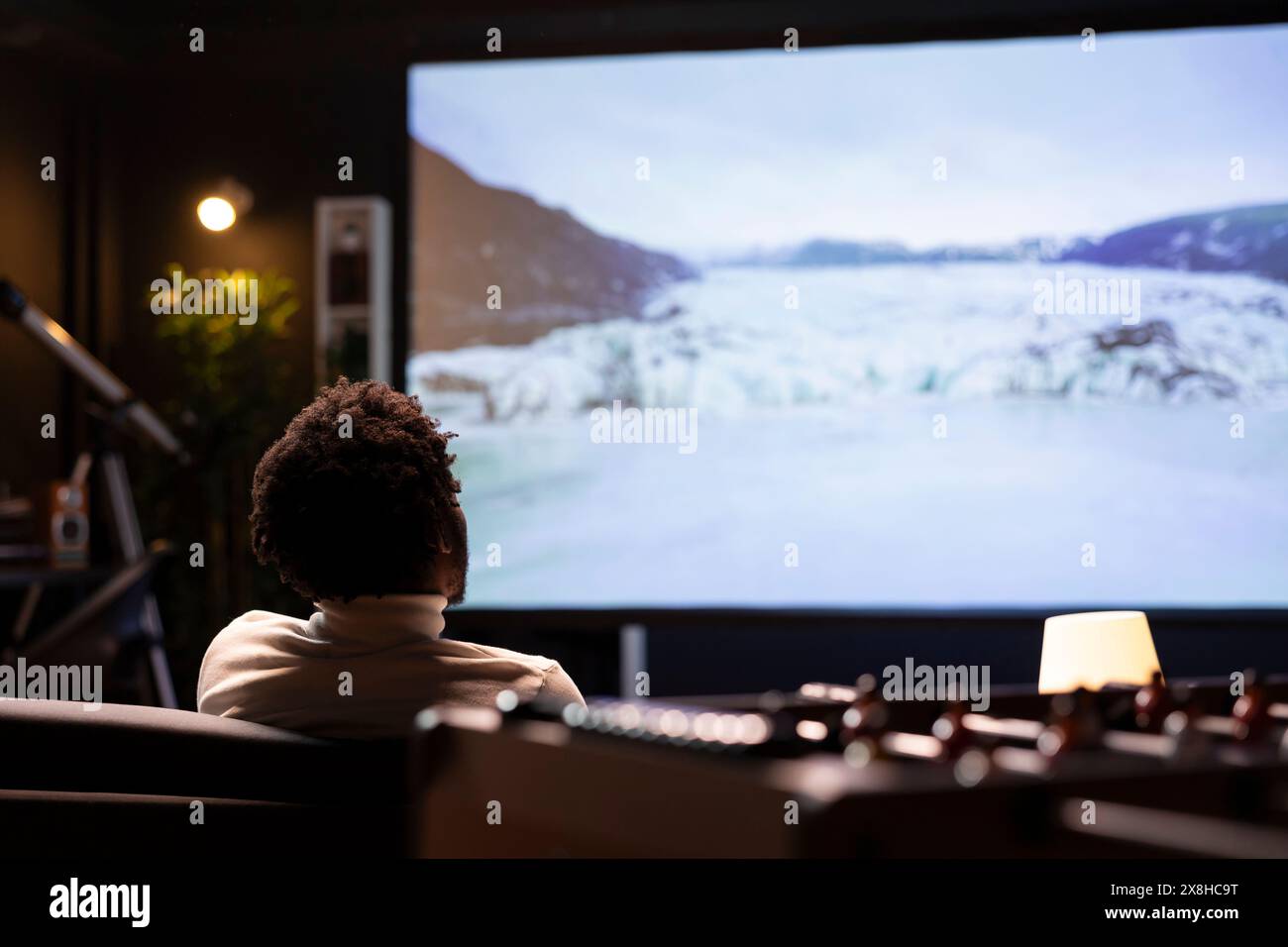 Tagliacavi ipnotizzato dalle clip naturalistiche online con splendide immagini cinematografiche sul display widescreen Smart TV. Uomo BIPOC che si gode di foto di paesaggi innevati pieni di ghiaccio sul canale VOD Foto Stock