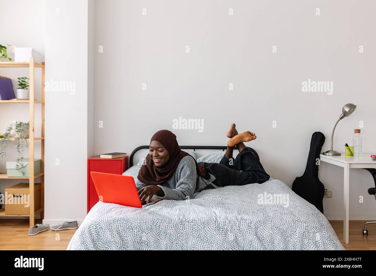 Giovane donna africana felice che scrive sul laptop mentre si sdraia a letto a casa Foto Stock