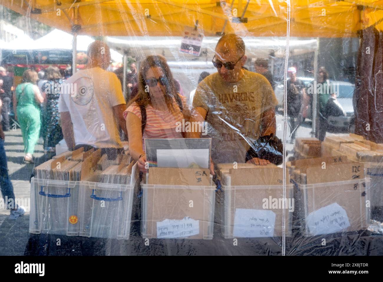 Coppia, fotografata attraverso fogli di plastica, curiosando in uno stallo del mercato del sabato a Grassmarket, Edimburgo, Scozia, Regno Unito. Foto Stock