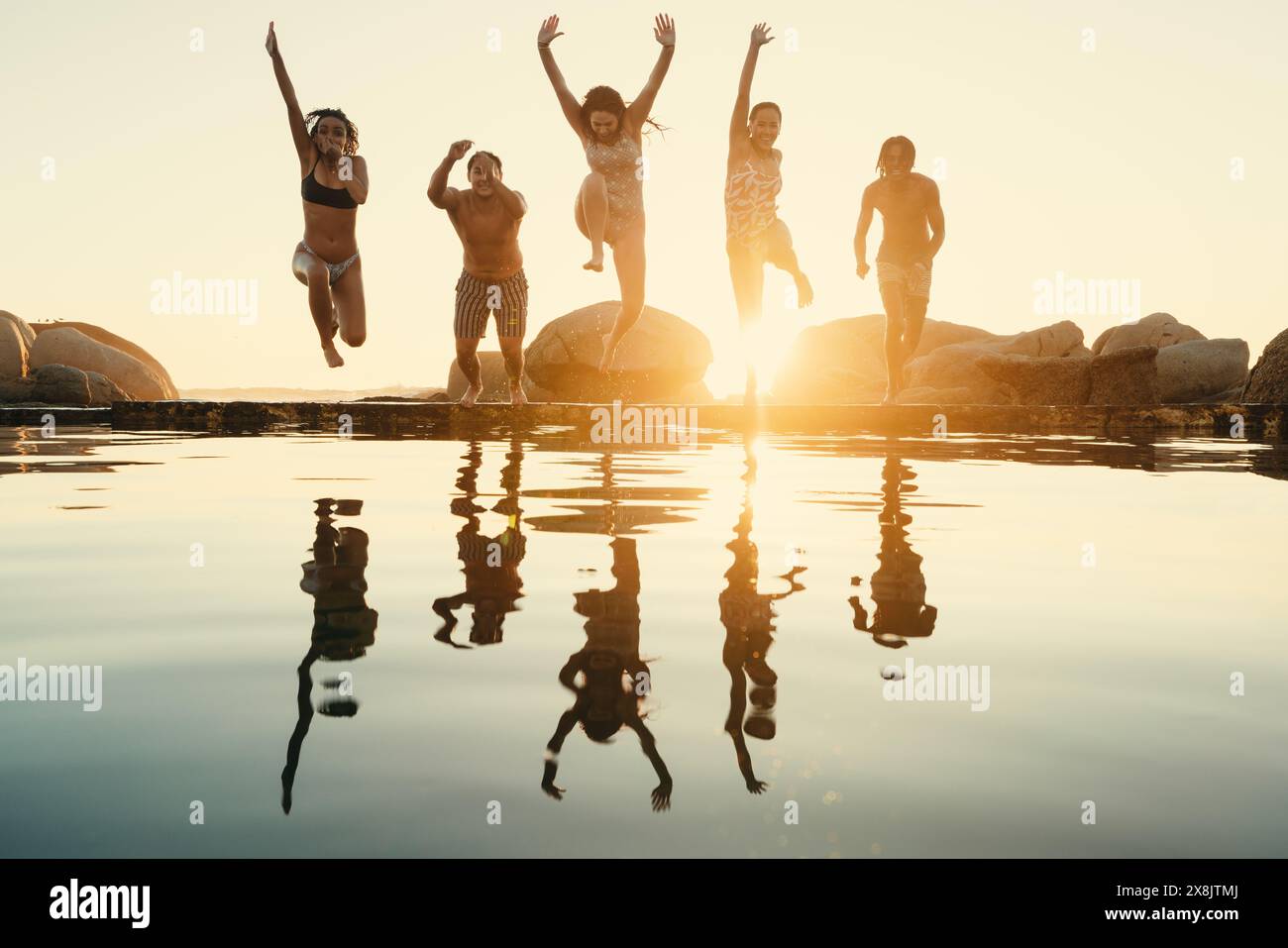 Un gruppo di amici si diverte e viaggia mentre saltano in acqua insieme al tramonto, riflettendo la loro gioia e cameratismo. Foto Stock