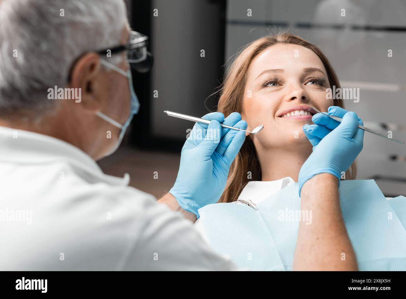 Un paziente è comodamente seduto sulla sedia dentale, il cui sorriso luminoso adorna l'ufficio. Il dentista si trova nelle vicinanze, pronto a fornire qualificati Foto Stock
