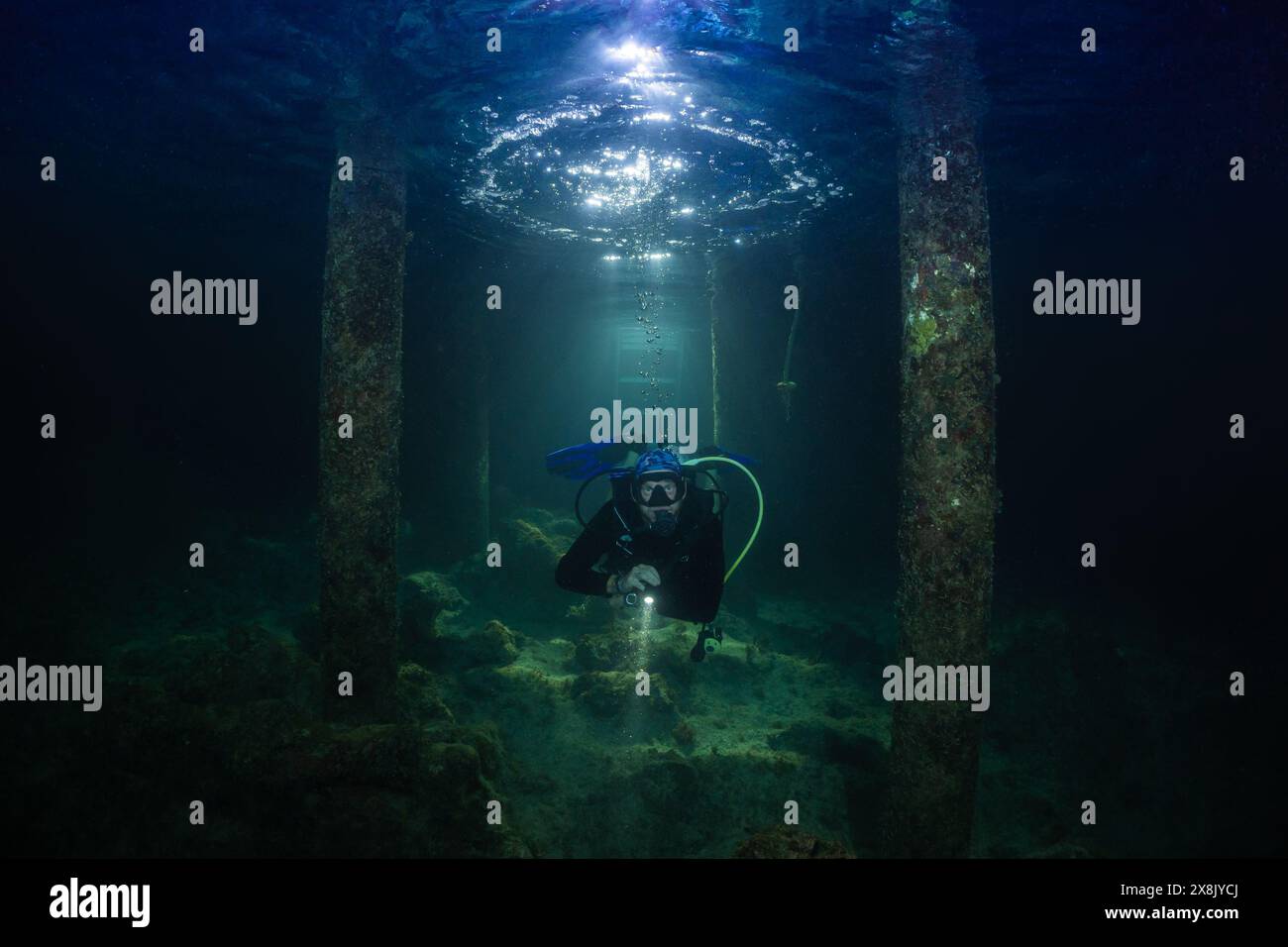 immersioni subacquee sotto un molo di notte. L'illuminazione sopraelevata cattura l'anello della bolla sulla superficie dell'acqua dall'espirazione Foto Stock