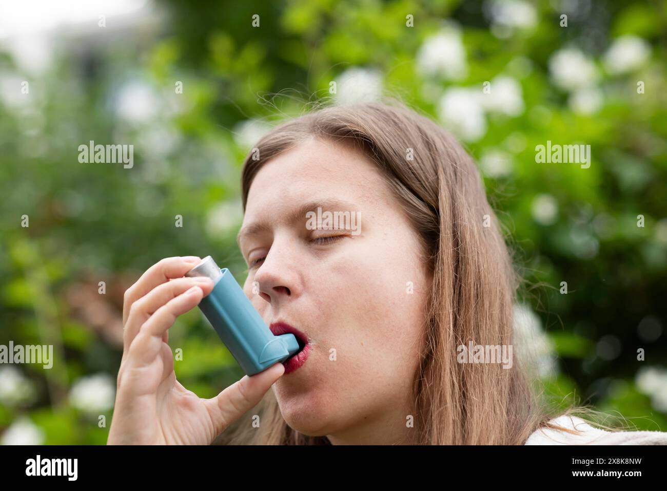 La giovane donna soffre di febbre da fieno e inala spray per l'asma all'aperto, Friburgo, Baden-Wuerttemberg, Germania Foto Stock