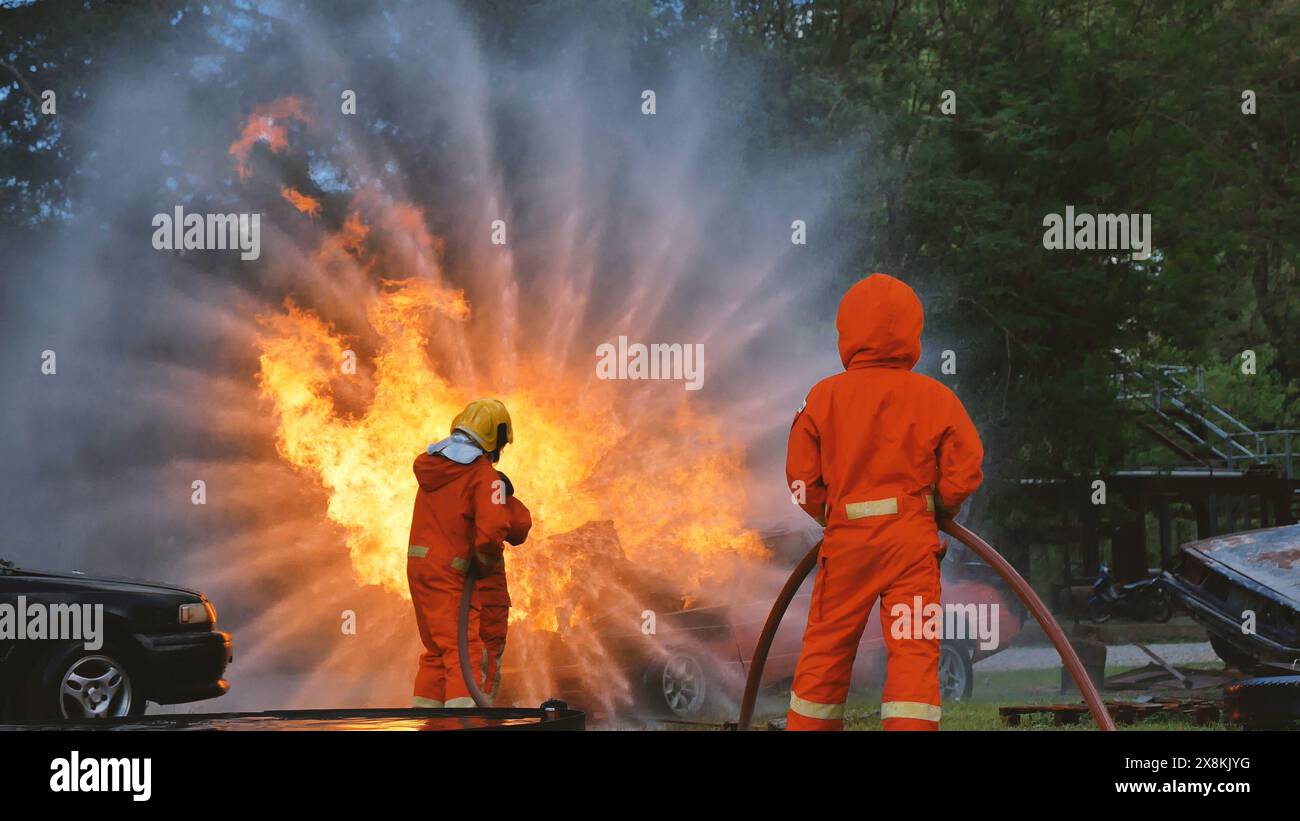 Vigili del fuoco che combattono con la fiamma utilizzando il tubo del fuoco il motore a spruzzo di schiuma chimica ad acqua. I pompieri indossano elmetto, uniforme per la protezione del corpo. Salvataggio Foto Stock