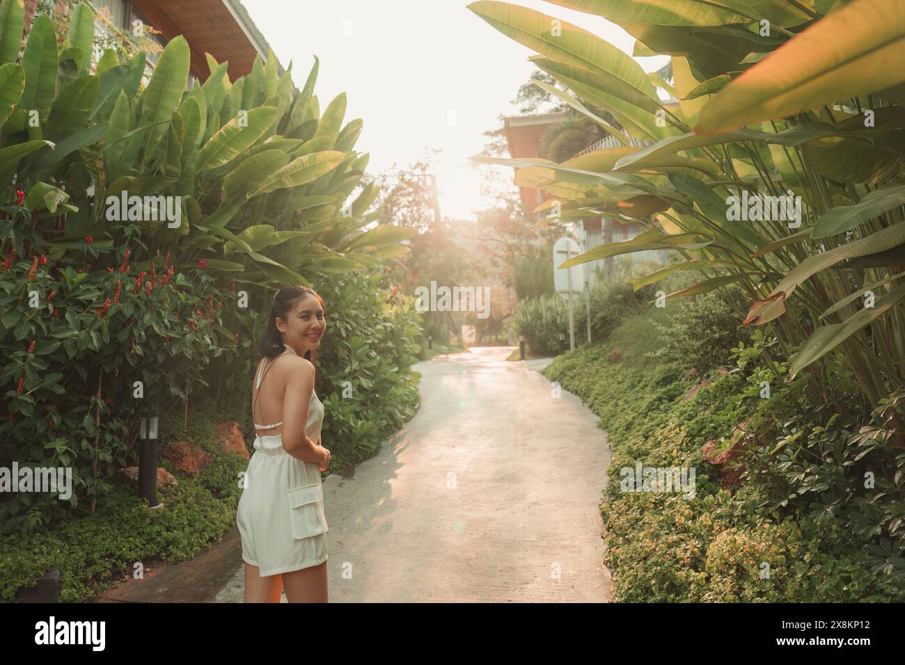 Bella, giovane donna asiatica che cammina e sorride nel giardino del resort tropicale Foto Stock