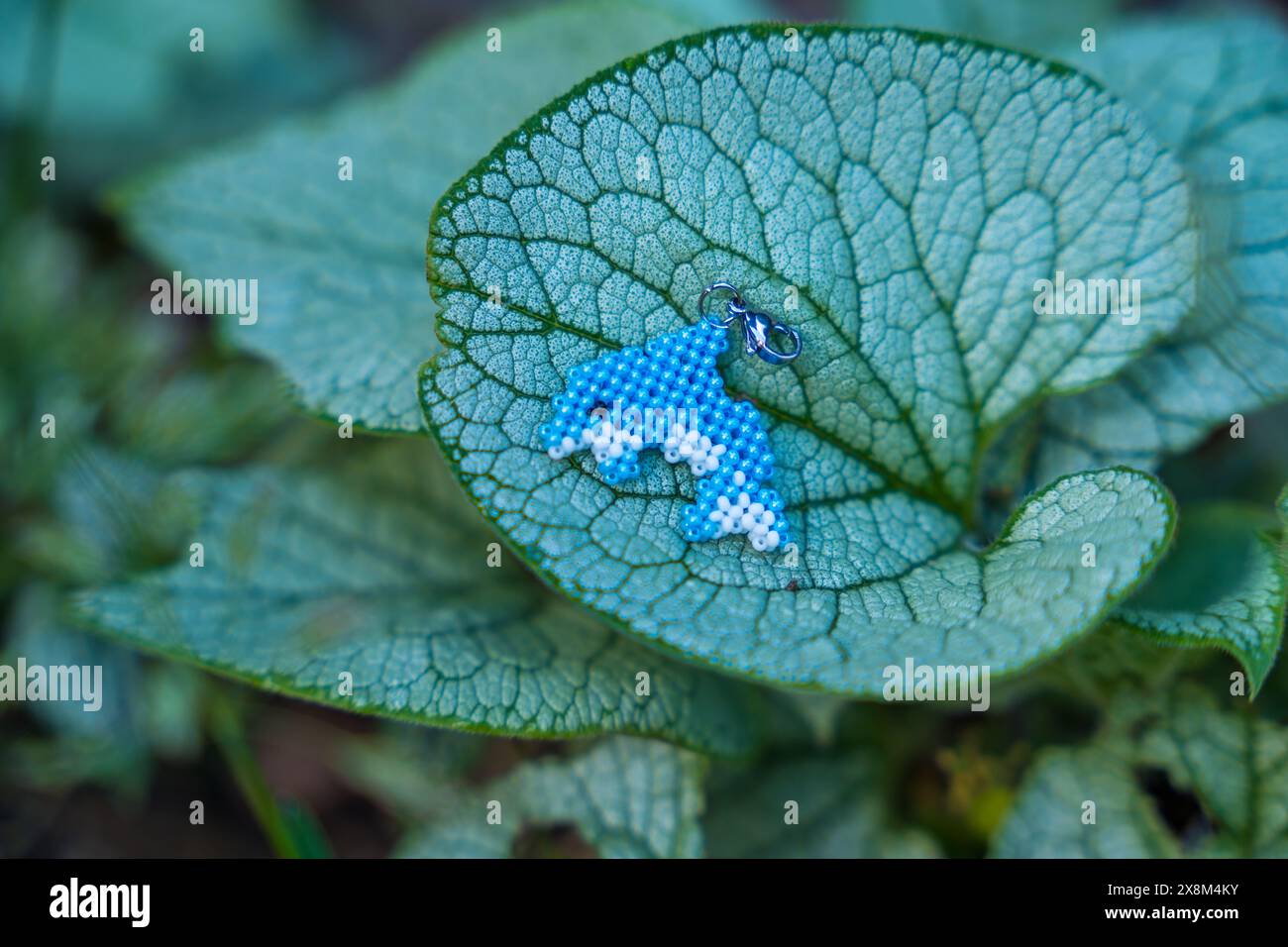 Un portachiavi di delfino con perline si trova su una grande foglia di piante vive in natura. Concetto artigianale. Foto Stock