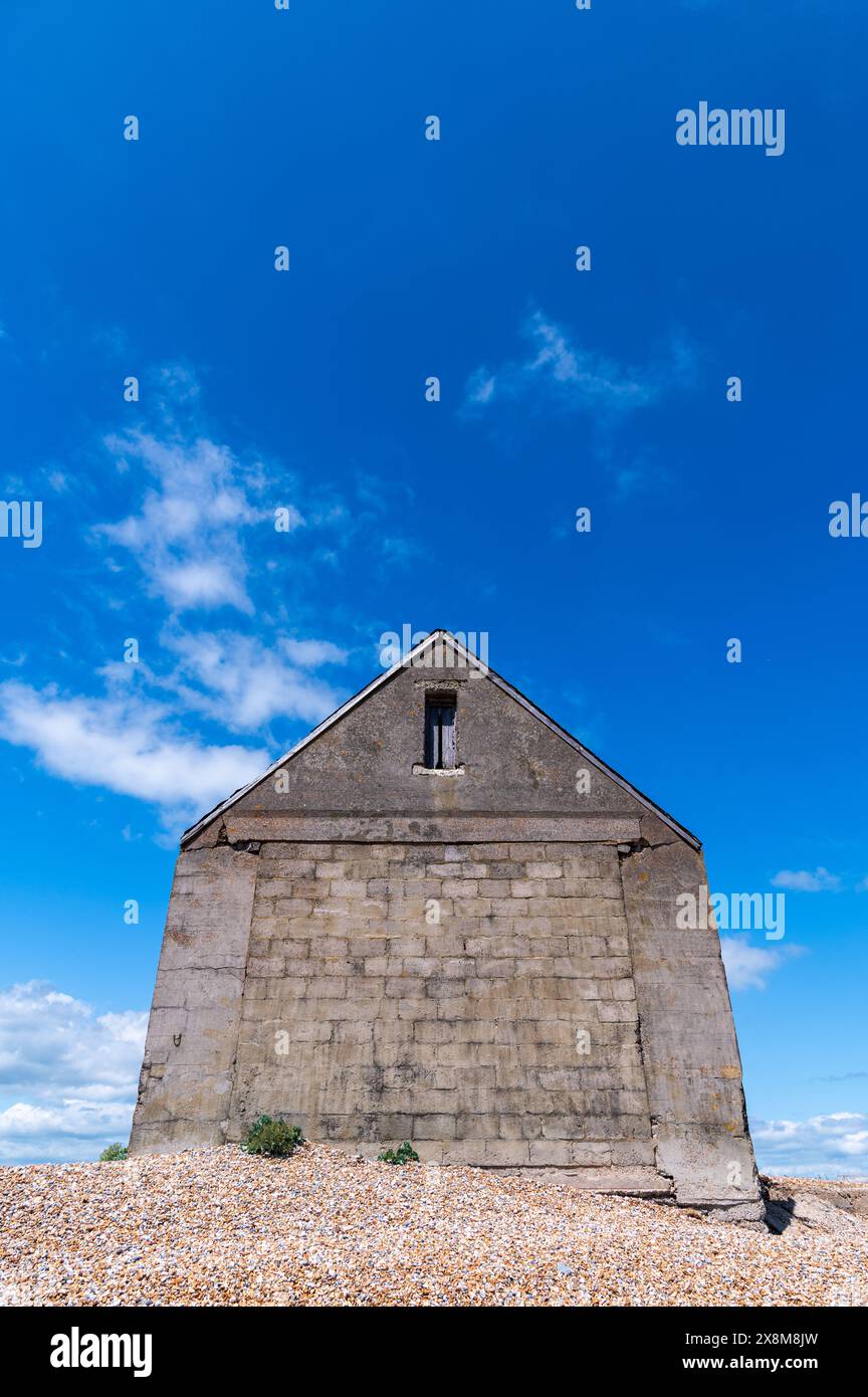 La Mary Stanford Lifeboat Station, abbandonata in cemento grigio, riserva naturale di Rye Harbour, in una giornata di sole con cielo blu intenso e nuvole bianche Foto Stock