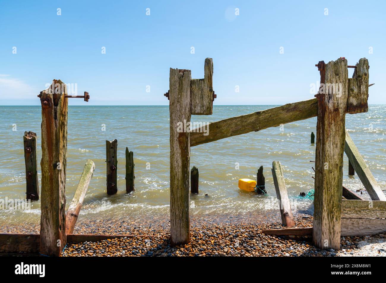 Tre vecchie e rotte difese marine in legno, paletti di groyne danneggiati, frangiflutti danneggiati nella riserva naturale di Rye Harbour in una giornata di sole Foto Stock