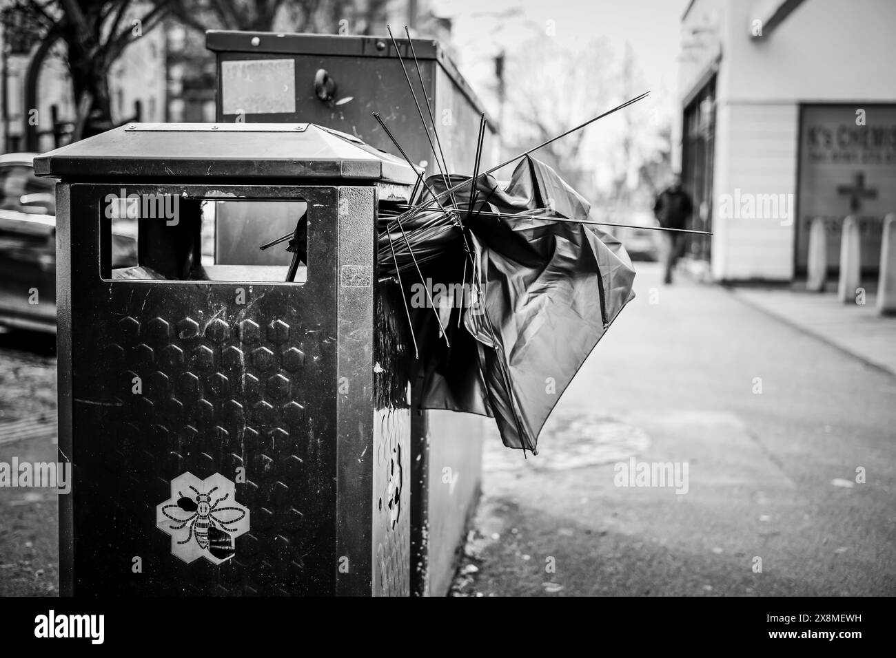 Manchester Regno Unito 26 marzo 2024. L'ombrello gettato fuoriesce dal bidone della spazzatura sul marciapiede della città, raffigurando i rifiuti urbani e lo stile di vita Foto Stock