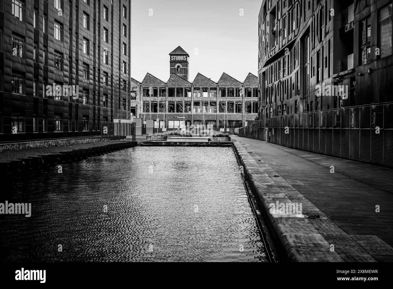 Manchester Regno Unito 26 marzo 2024. Paesaggio urbano bianco e nero con un vecchio edificio industriale tra strutture moderne, tranquillo corso d'acqua in primo piano Foto Stock