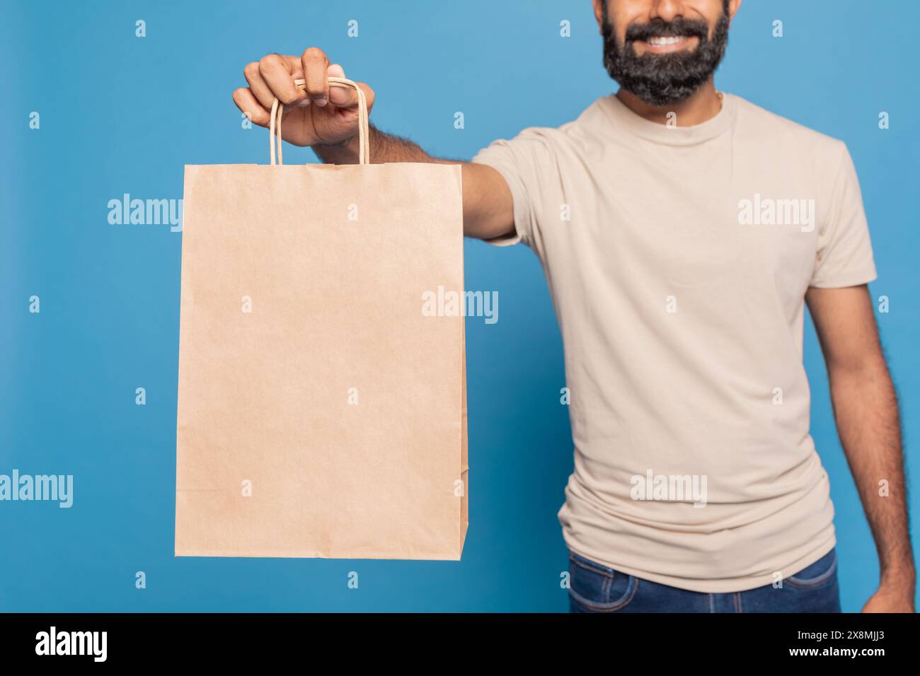 Uomo sorridente che tiene in mano un sacchetto di carta marrone su sfondo blu Foto Stock