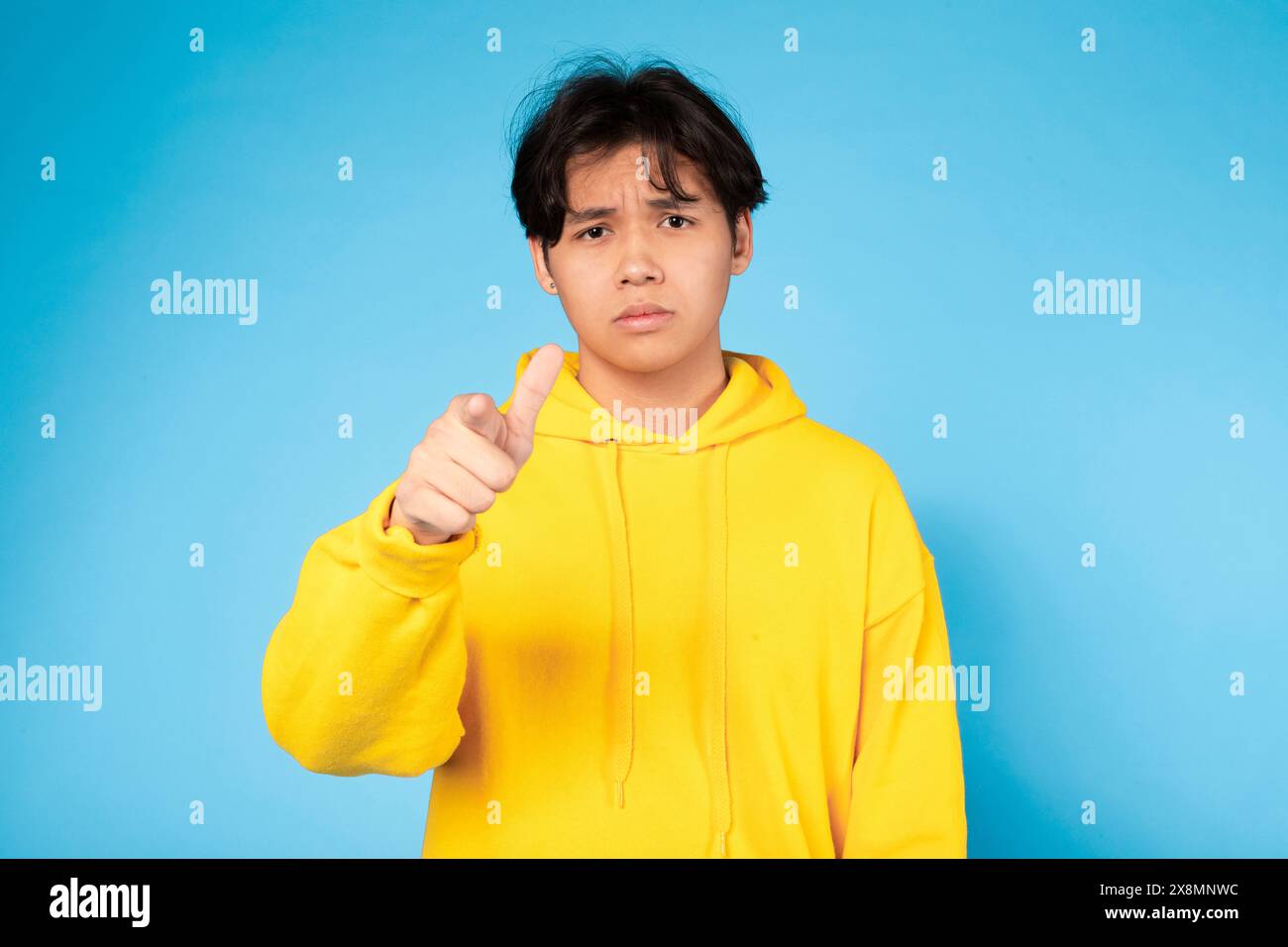 Giovane ragazzo con cappuccio giallo che punta in avanti contro Blue Foto Stock