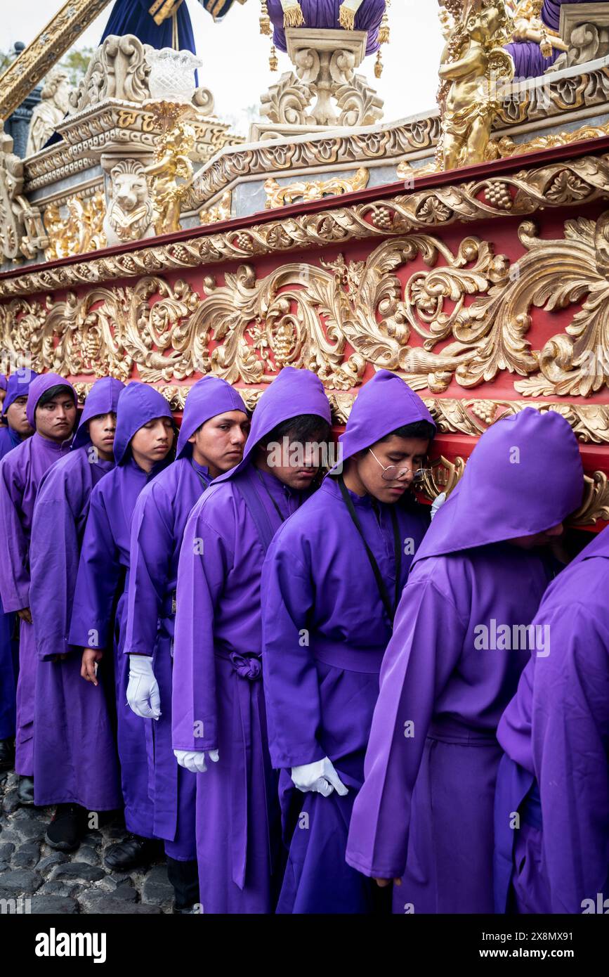 Primo piano di giovani uomini e ragazzi vestiti di monaci viola che si prendono cura della statua di Gesù, tradizionale processione di Pasqua, Antigua, Guatemala Foto Stock