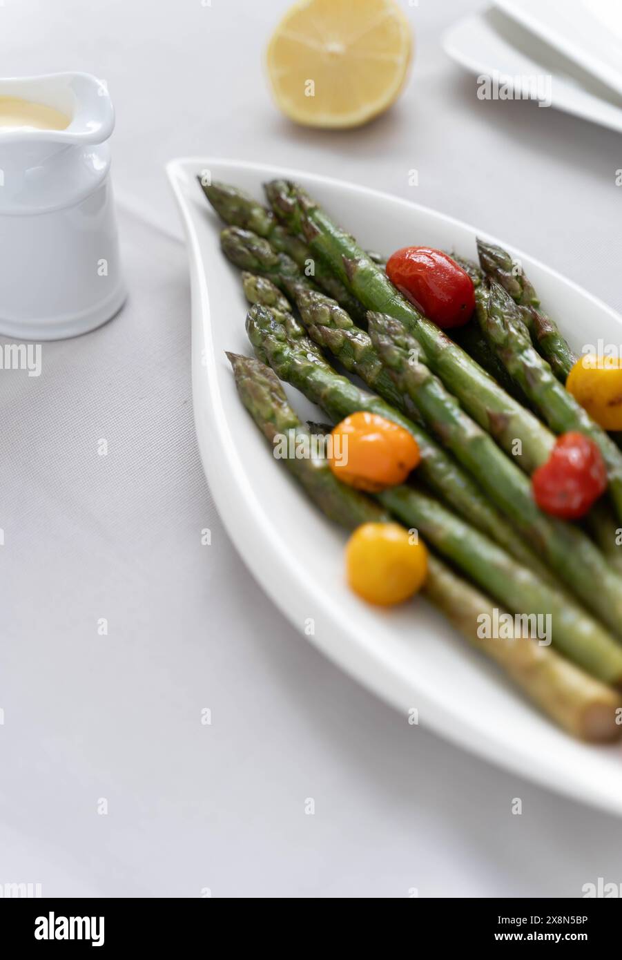 Fonte di grande fibra alimentare, asparagi verdi cotti al forno serviti in un piatto bianco, preparato come contorno con pomodori colorati Foto Stock