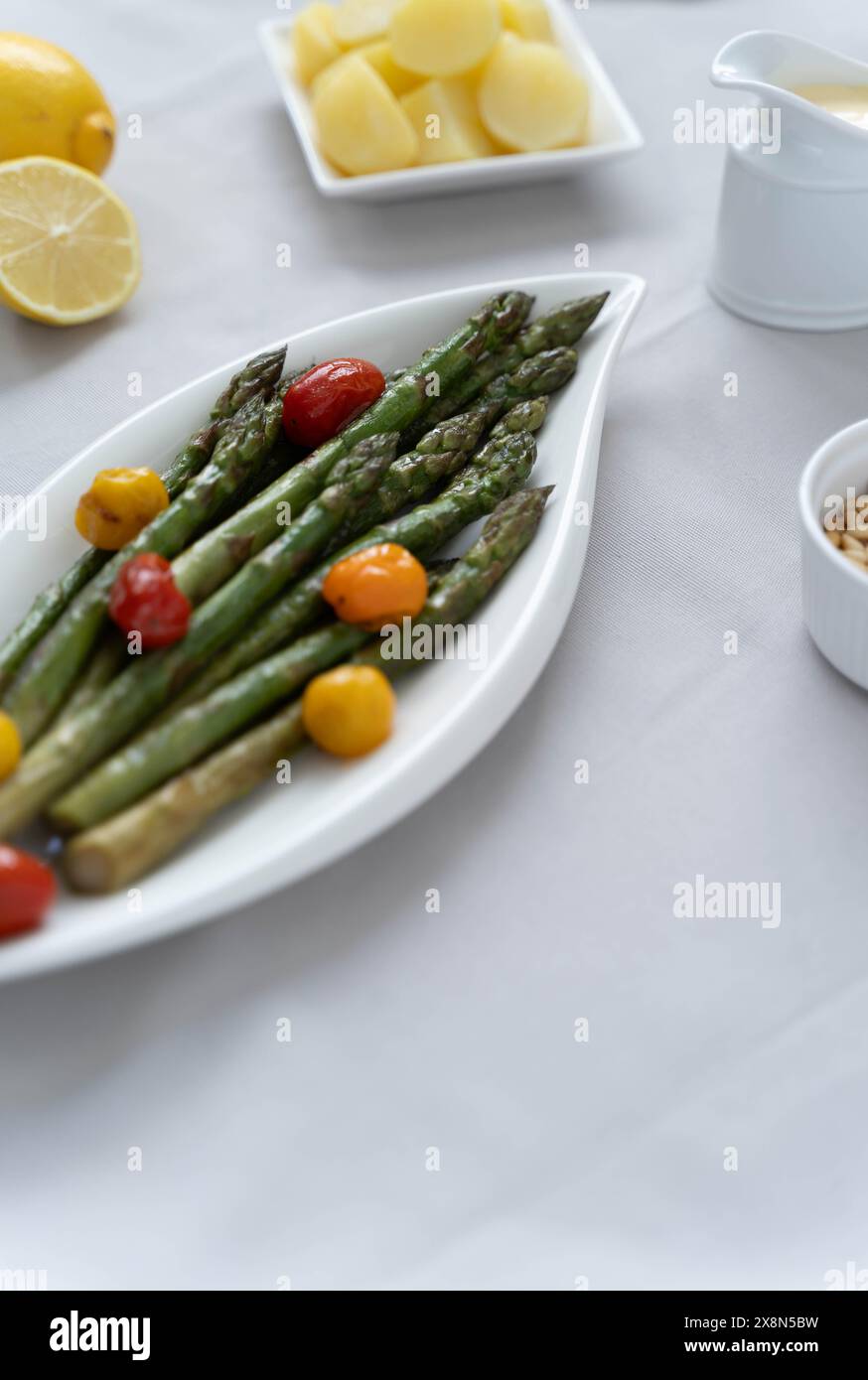 Fonte di grande fibra alimentare, asparagi verdi cotti al forno serviti in un piatto bianco, preparato come contorno con pomodori colorati Foto Stock