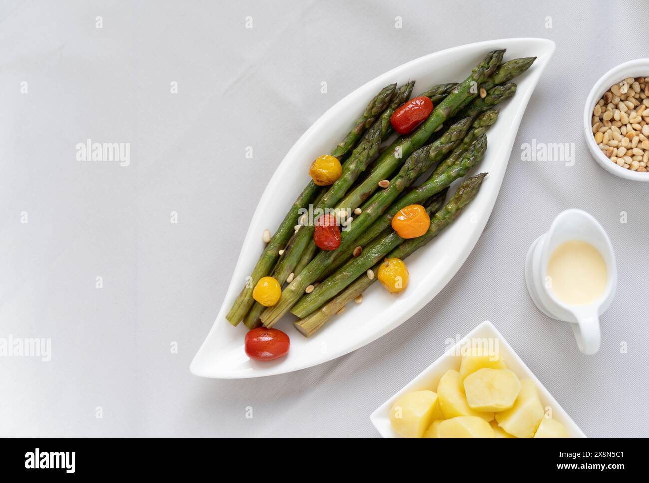 Fonte di grande fibra alimentare, asparagi verdi cotti al forno serviti in un piatto bianco, preparato come contorno con pomodori colorati Foto Stock