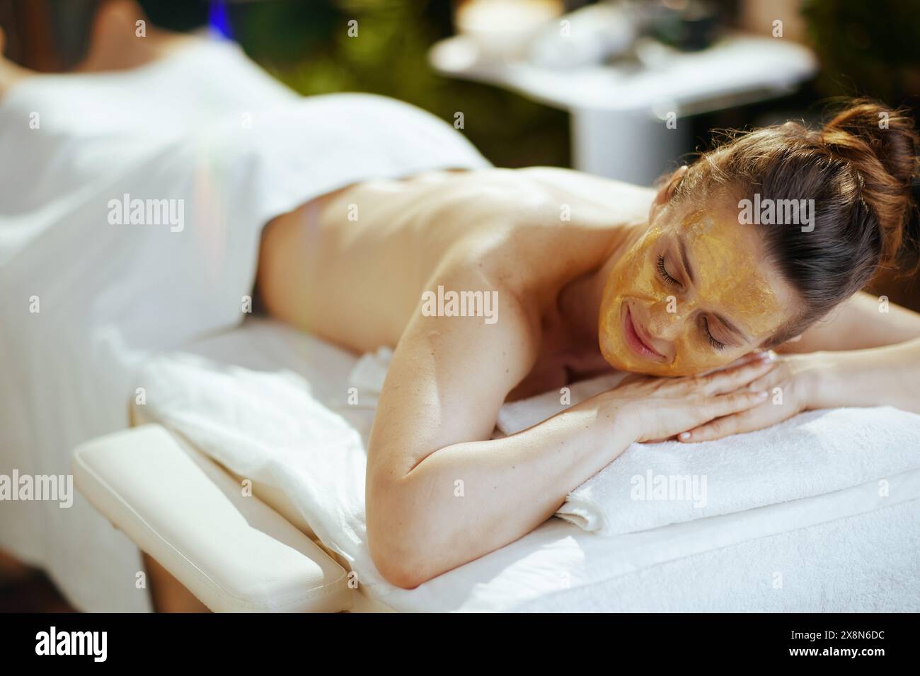 Il tempo dell'assistenza sanitaria. donna moderna e rilassata nel salone spa con maschera cosmetica dorata sul viso appoggiata sul tavolo da massaggio. Foto Stock