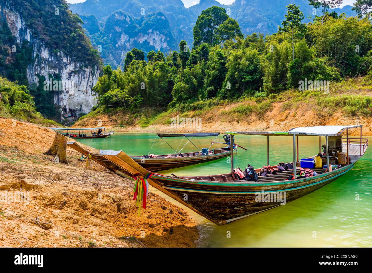 Barche a coda lunga sulla riva di un lago della foresta pluviale con torreggianti scogliere calcaree alle spalle Foto Stock