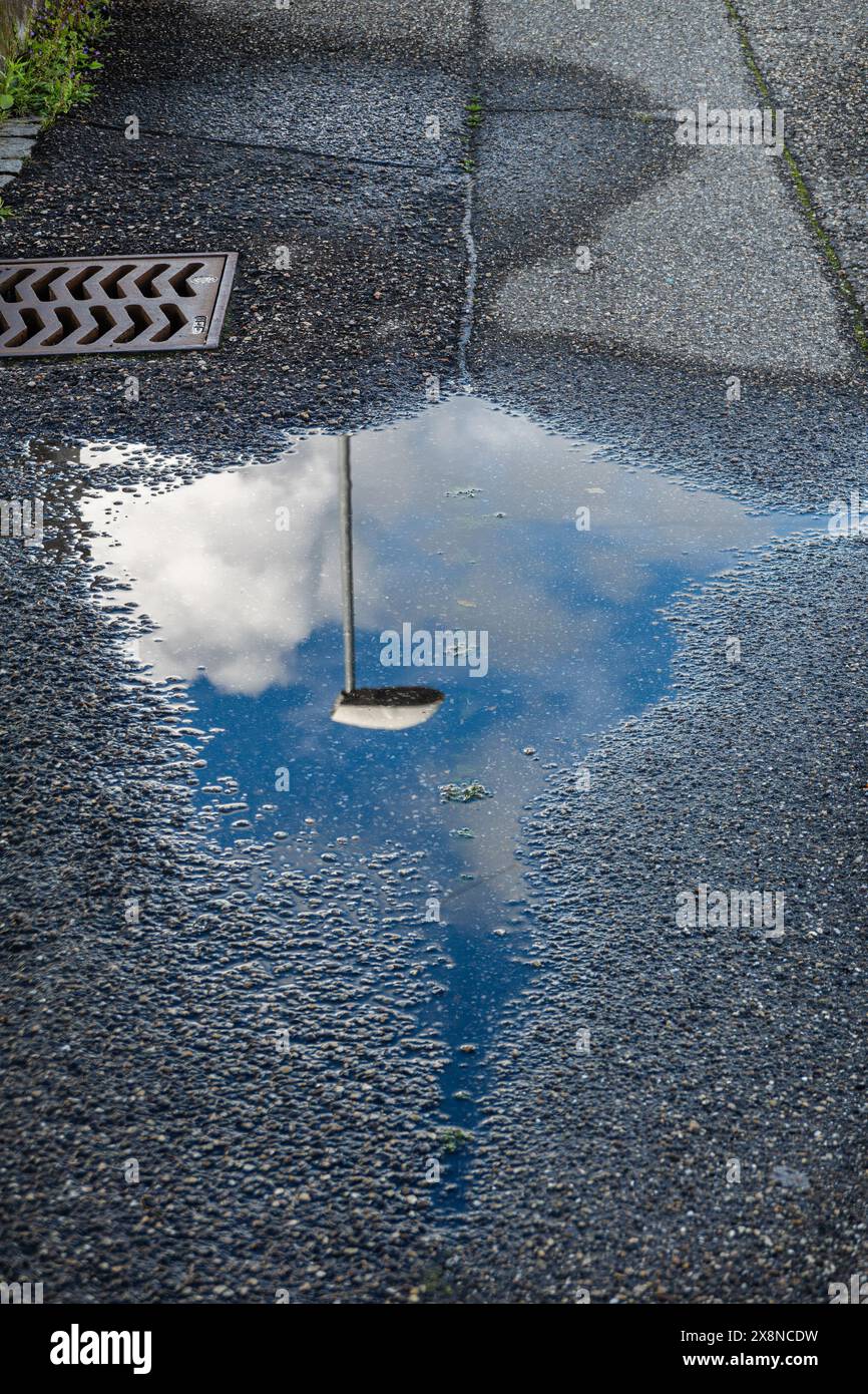 Bagnomaria su asfalto ruvido. Riflesso di lampione, cielo, nuvole. Illusione artistica di fondere elementi. Foto Stock