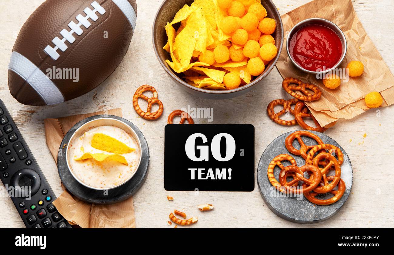 Spuntini per guardare una partita di football americano. Birra, patatine, pretzel, salsa su fondo di legno. Vista dall'alto Foto Stock