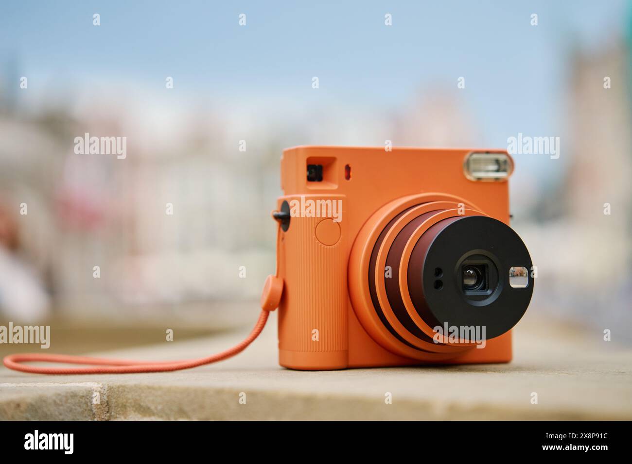 Fotocamera Orange Instant vintage in città con cielo nuvoloso. Attrezzatura da tiro da viaggio Foto Stock